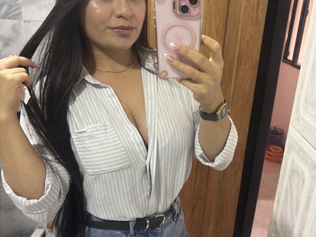 MiaDuboisX with long black hair, striped shirt, and blue jeans, holding phone, showing her tits in mirror, pink phone case, gold watch, and black belt in bathroom.