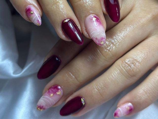 MiaDuboisX's glossy nails are a mix of deep burgundy and pink with white swirls, gold dots, and tiny pink flowers on the tips, showing off her shiny, manicured hands.