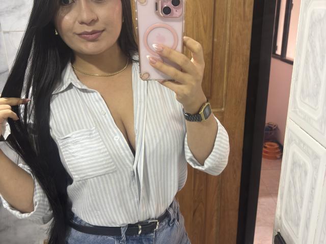 MiaDuboisX with long black hair, wearing a striped shirt, showing her cleavage, holding her hair, wearing a gold necklace, and a watch, taking a mirror selfie.