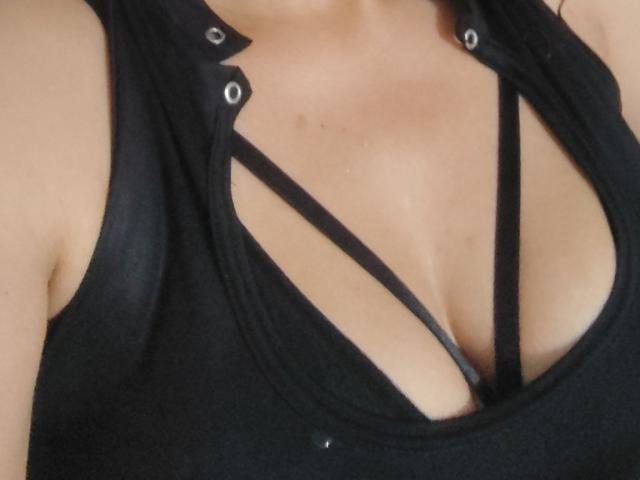 VioletaSwitch's black tank top has strappy black lines cutting across her tits, showing a deep cleavage with her large, round breasts. Her skin is light and smooth.