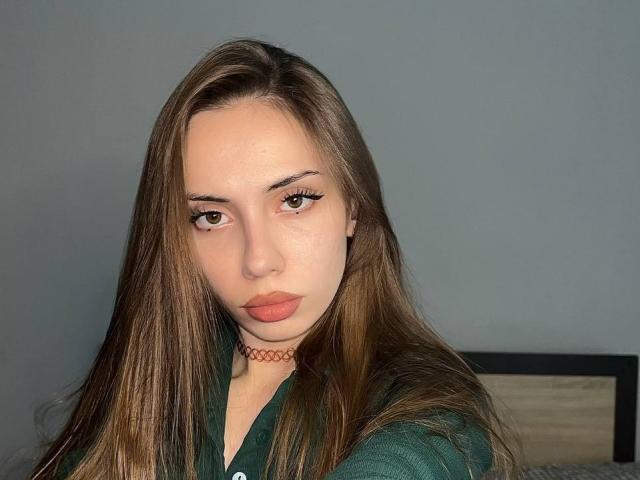 JudyPalas tem cabelos castanhos longos, olhos verdes e um colar vermelho, vestindo uma camisa verde, com lábios cheios e uma expressão neutra. Seus seios são pequenos..