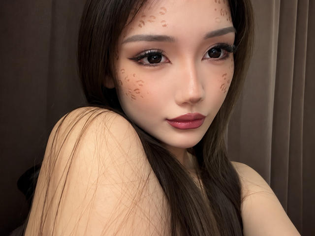 ShontaPasserino has long brown hair, dark eyeliner, and brown freckles on her face. She's looking at the camera with pink lips, wearing a sleeveless top.