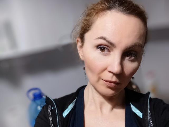 TessBertie has light brown hair, brown eyes, and a slight smile. She's wearing a black jacket with blue trim, and a blue water bottle is in the background.
