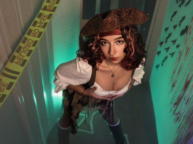 KanelaMiller with curly brown hair, wearing a brown tricorn hat, white puffed sleeves, low-cut dress, black stockings, and a cross necklace, looking up with large tits, in a hallway.