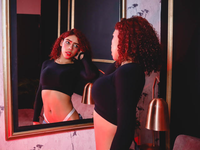 ValerieMartin with curly red hair, black long-sleeve crop top, and white panties, standing in front of a mirror, holding a phone to her ear, looking at her reflection.