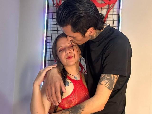 GraceAndTony with her red mesh top, tits visible, and Tony, tattooed and in a black shirt, kissing her forehead. Tony's hand on her ass, both smiling.