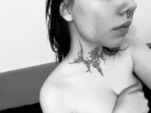 MariannaWarren with a tattoo of branches and flowers on her neck, topless, nose ring, and wet dark hair, showing her shoulder and part of her boob. Black-and-white photo.