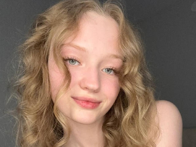 BulahLiebman has wavy blonde hair, blue eyes, and a subtle smile with pink lips, showing fair skin and natural makeup. Her tits aren't visible.