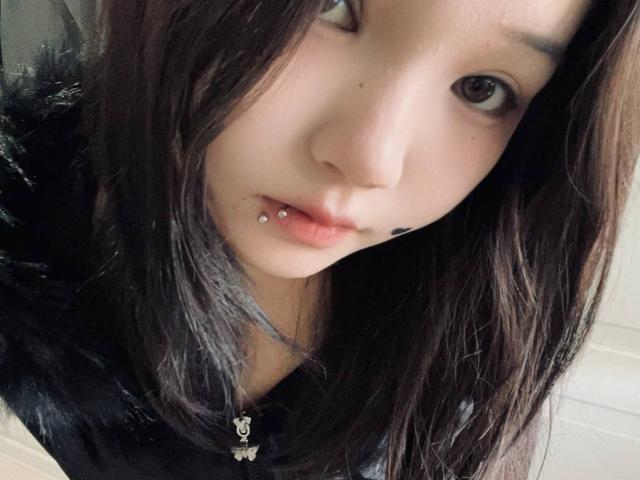 RayeAbend's face with straight, dark brown hair, light skin, and a small black nose ring in her lower lip. She has a slight, curious expression and brown eyes.