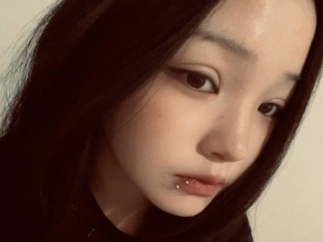 RayeAbend has pale skin, black hair, brown eyes, and a lower lip piercing. She looks down with a slightly sad or contemplative expression in a soft, muted photograph.
