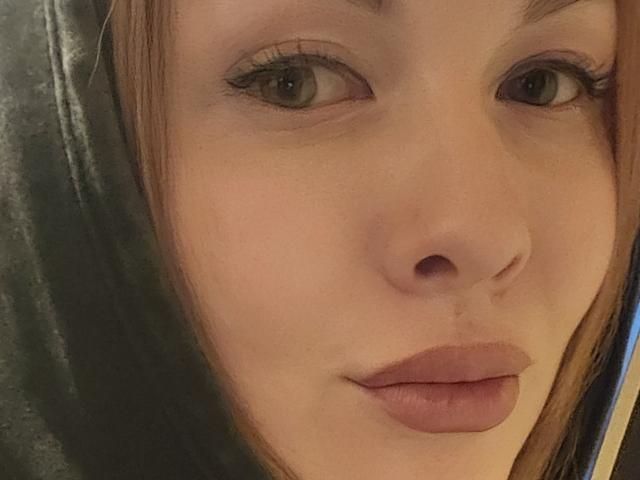 O rosto de KatrinaSi, mostrando seus olhos verdes, cabelo castanho e lábios rosados, com um delineador discreto e um sorriso leve e relaxado. Seu nariz é pequeno e sua pele é clara..