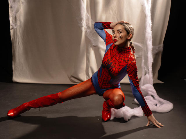LettieSweet in a Spider-Man costume, crouching with one knee on the floor, wearing red boots and a blue-red Spider-Man suit, showing her ass and a seductive look.
