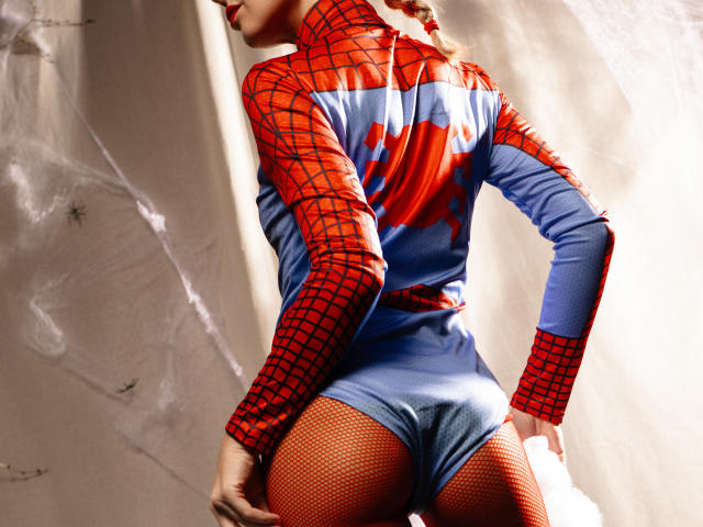 LettieSweet in a red and blue Spider-Man suit, showing her ass in fishnet stockings, standing with her back to the camera, her hair in a braid.