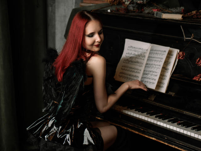 MarieLoving with red hair, black feathered wings, and black dress, playing a piano, showing her tits, smiling, looking over shoulder. Dark, moody, sexy.