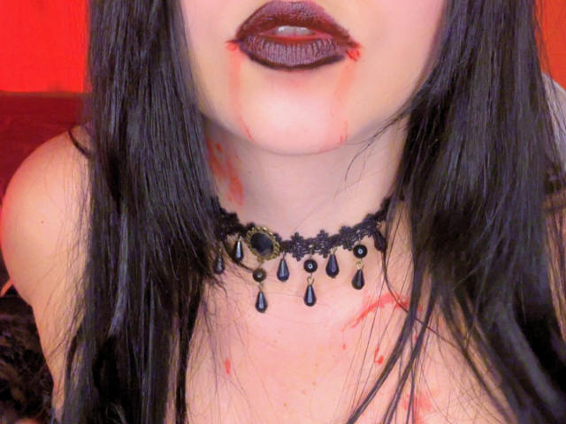 Kkatalina with bloody lipstick, dark hair, black lace choker, black teardrop beads, and blood on her neck and chest, showing her bare shoulders and upper tits.