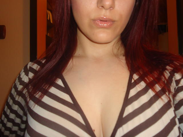 DouceAnna with shiny pink lips, red hair, and a striped brown and white shirt, showing her big boobs and cleavage. She's looking down, slightly pouty.