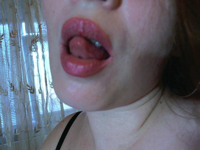 VictoriaSecrets' face, showing her pinkish-red lips and tongue slightly out, with a black strap visible on her shoulder. Her skin is pale with a slight red blush.