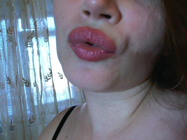 Das Gesicht einer Victoria's Secret Model, mit vollen, rosa-roten Lippen, die leicht geöffnet sind, heller Haut, braunen Haaren, einem schwarzen Träger und einem zarten Hals. Nahaufnahme, sie zieht die Lippen leicht zusammen, mit weichem Licht..