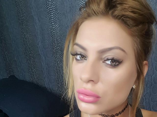 MissKhloe's face with pink glossy lips, brown eyes, and thick eyelashes. She has blonde hair in a messy updo, dark eyebrows, and a black choker. Boobless, no visible ass.