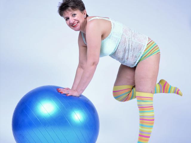 DoraBlueEyess, short brown hair, white lace top, yellow-striped thigh-highs, green shorts, blue exercise ball, smiling, bending over ball, hands on top, legs bent, background white.