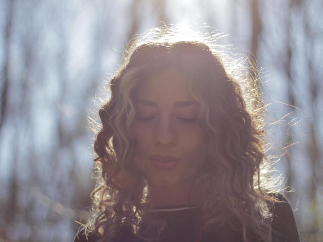 PoxyVibe heeft golvend blond haar, met highlights in haar gezicht, haar ogen zijn gesloten en ze heeft een zachte, vredige uitdrukking. Ze draagt een donkere top, en haar achterkant is niet zichtbaar..