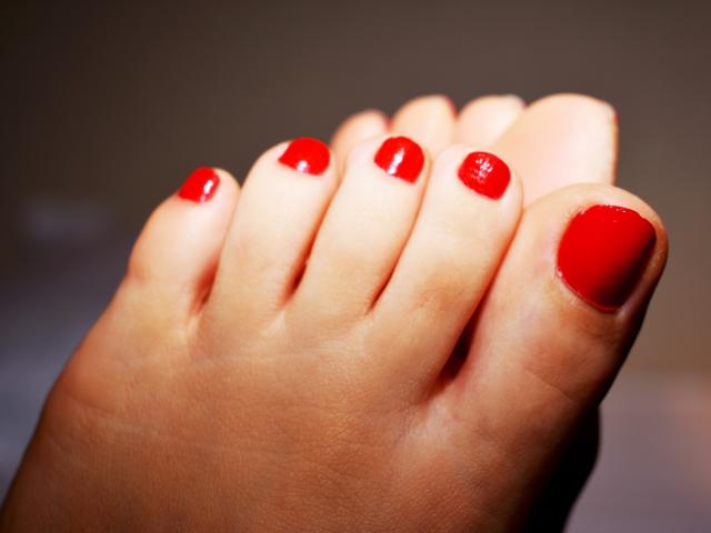 Le dita dei piedi di GinnyGold, dipinte di un rosso brillante con uno smalto liscio e lucido, presentano una pelle ben curata e pulita, e una posizione leggermente arcuata delle dita..