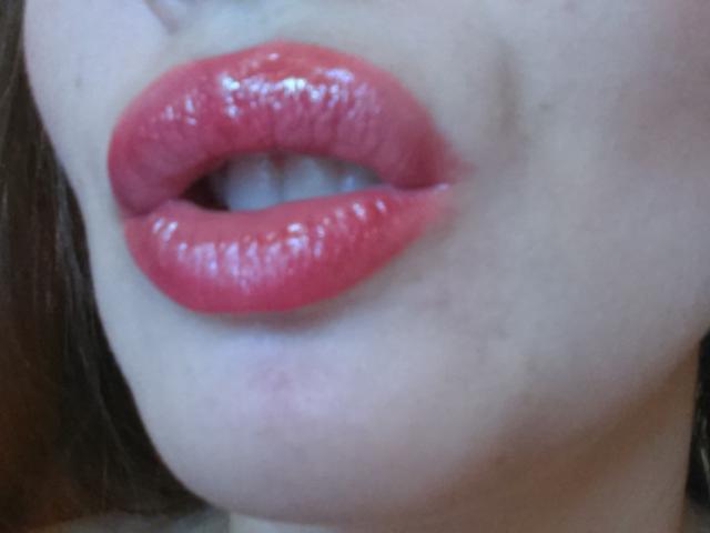 Le labbra rosa lucide di Victoria's Secret, leggermente dischiuse per rivelare un accenno di denti bianchi, con una carnagione chiara e delicata e una texture della pelle sottile..
