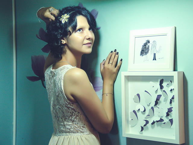 AmethystCharm with dark curly hair, white lace dress, black nails, flower in hair, looking over shoulder, standing against green wall, touching framed art. Pussy is not visible.