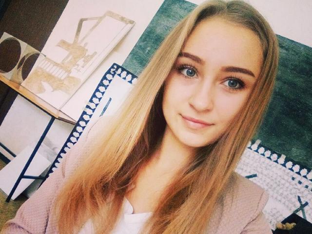 MerindaFoxy a de longs cheveux blonds, des yeux bleus et un léger sourire. Elle porte un cardigan rose par-dessus une chemise blanche. Ses seins sont petits, et elle est mignonne..