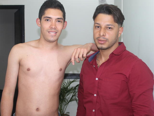 LiamXThom senza camicia, con un leggero sorriso, un braccio attorno a LiamXThom che indossa una camicia rossa; entrambi hanno capelli corti e scuri; LiamXThom a sinistra, LiamXThom a destra, corporatura media..