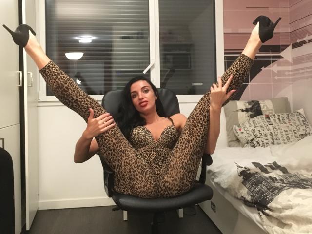 KatieFrenchie in a leopard-print bodysuit with her legs spread wide, black high heels, and red lipstick, sitting in a black chair, showing off her pussy and tits.