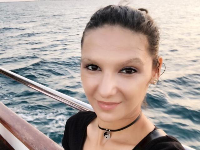 AmethystCharm has a cute smile, brown eyes, and a black choker with a small key pendant. She's wearing a black top and has her dark hair in a bun.