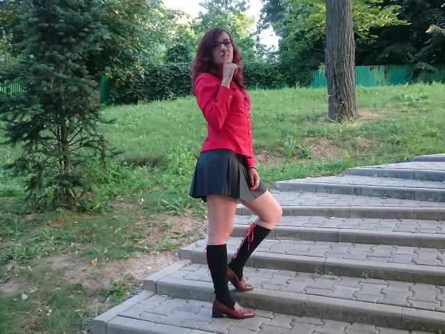 MoonBlossom standing on stone steps, wearing a red shirt, black skirt, grey shorts, black knee socks, brown boots, and glasses, with one hand near her mouth.