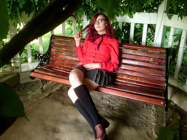 MoonBlossom with red shirt, black skirt, and knee socks, sitting on wooden bench, holding cigarette, glasses, and brown shoes, showing her tits and ass, in greenery.