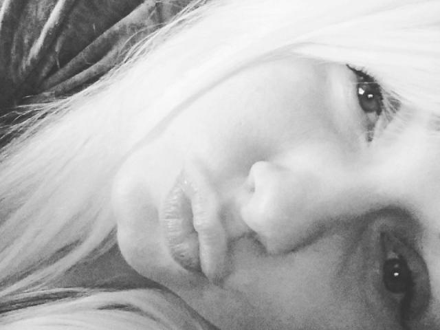 El rostro de PinkDevil en una fotografía en blanco y negro, mostrando labios fruncidos y una nariz pequeña, con cabello rubio y un pendiente visible en su oreja derecha, mirando ligeramente hacia la izquierda..