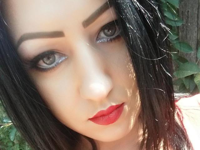 BeauxYeuxx's face with dark eyebrows, glittery eyes, and red lipstick. Black hair, light skin, and a subtle shadow on the right side. BeauxYeuxx's eyes are blue-gray.