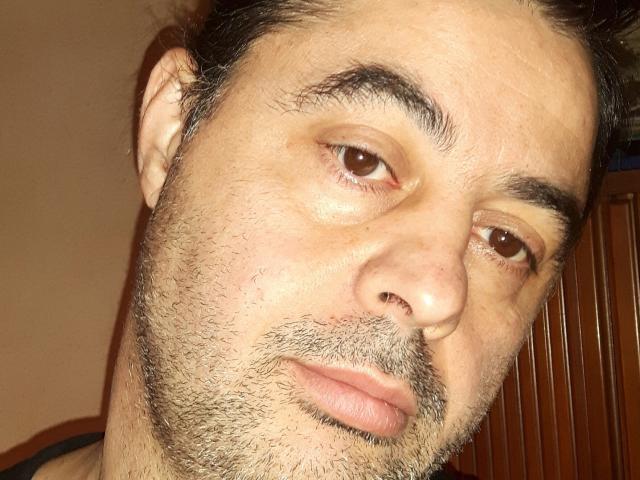 A photo of sweetpenis with a slightly tilted head, brown eyes, dark eyebrows, and a short beard, looking off to the side with a neutral expression.
