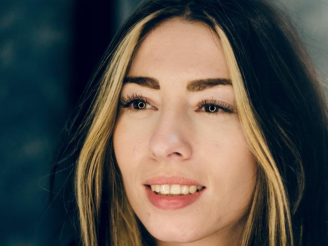 PoxyVibe has blonde and brown hair, light skin, brown eyes, and is smiling with her teeth slightly visible. Her makeup includes long eyelashes and pinkish lips.
