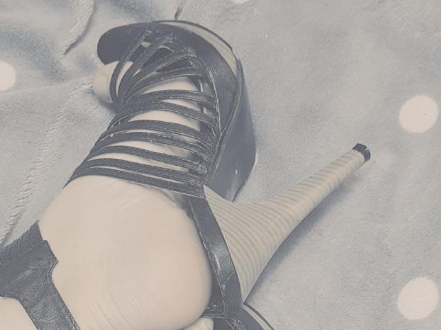 LovelyMichellex69's foot in a black strappy high heel with a thick sole, wearing a striped sock, showing a slight heel bruise and textured fabric underneath.