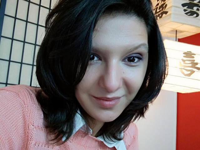 AmethystCharm has medium-length black hair, a cute smile, and light skin. She's wearing a pink knit sweater with a white collar, looking directly at the camera.