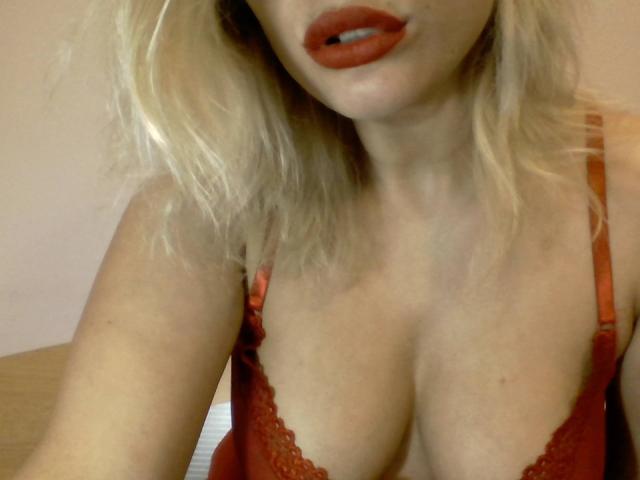 Eilly with blonde hair, red lipstick, and red lace bra, showing her tits, slightly open mouth, and fair skin. Her boobs are medium-sized with visible cleavage.