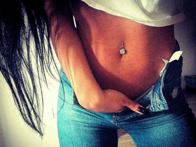 Azazelle's taut, tan midriff with a belly button piercing, wearing unbuttoned blue jeans, her hand in the waistband, long black hair falling over her shoulder.