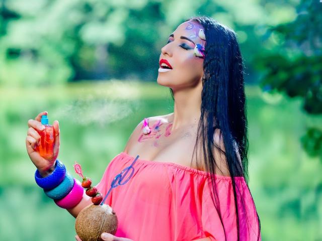 RoseCream con cabello negro, top rosa con un hombro descubierto, maquillaje facial colorido, lápiz labial rojo, pulseras azules y rosas, sosteniendo polvo naranja, sonriendo, fondo verde borroso. Pechos, maquillaje facial, polvo..