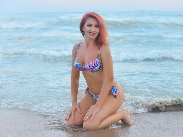 IvyFox, kneeling on a beach, wearing a colorful striped bikini, has pink hair, small tits, and a cute smile, with orange nails, and a sexy, attractive look.