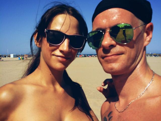 CassandraFredStyler mit kleinen Brüsten, die dunkle Sonnenbrillen trägt, und CassandraFredStyler mit einem kahlrasierten Kopf, grünen Pilotenbrillen und einer schwarzen Mütze, beide ohne Hemd am Strand..