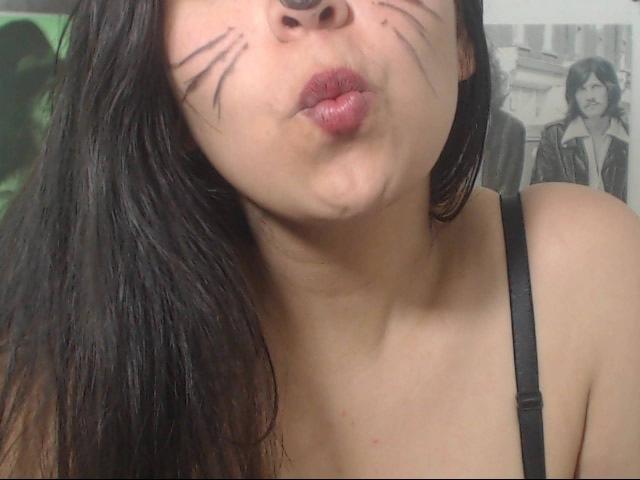 SharickPoilu with black whisker makeup, puffy lips, and black hair, wearing a black strap, looking up with a pouty face, showing her tits and nose ring.