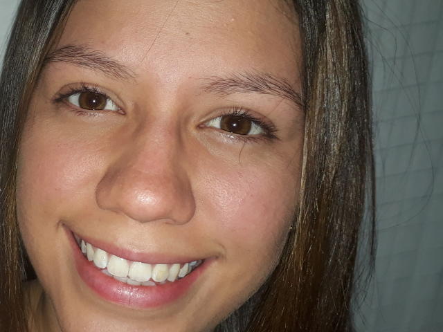 O rosto de PinkSexyX, mostrando olhos castanhos, cabelo castanho liso, lábios rosados, dentes brancos e um leve sorriso. Ela tem pele castanha clara e sobrancelhas visíveis..