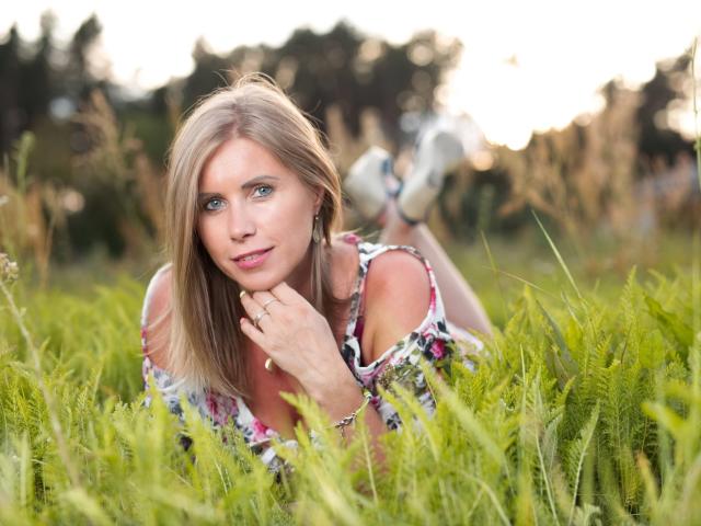 DoorenHot with blonde hair, blue eyes, floral dress, lying in green grass, hand on chin, white sneakers, looking at camera, soft sunlight, cute, pretty, ass slightly raised.