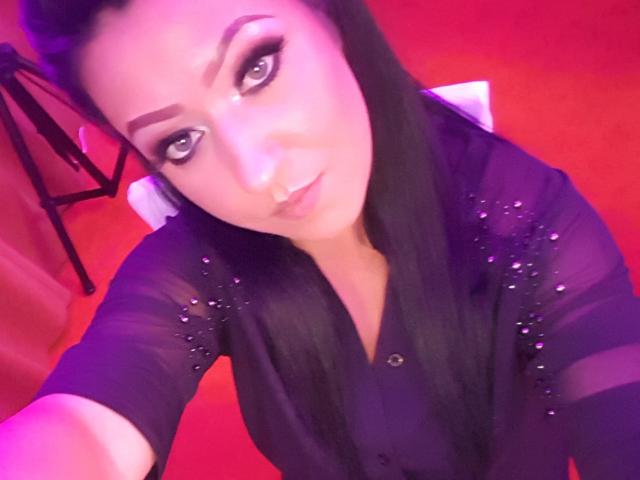 BeauxYeuxx, met zwart haar, draagt een doorschijnend zwart topje met glitters, heeft een neusring en eyeliner, kijkt naar de camera, met een paars-rode lichteffect..
