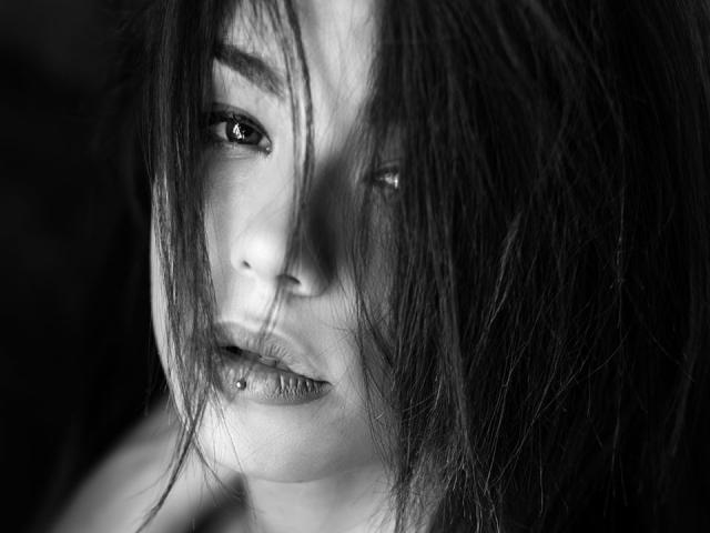 KassiKassou a les cheveux noirs et emmêlés qui lui cachent les yeux, une bouche légèrement ouverte avec une lèvre inférieure percée, et une expression sérieuse sur une photo en noir et blanc..